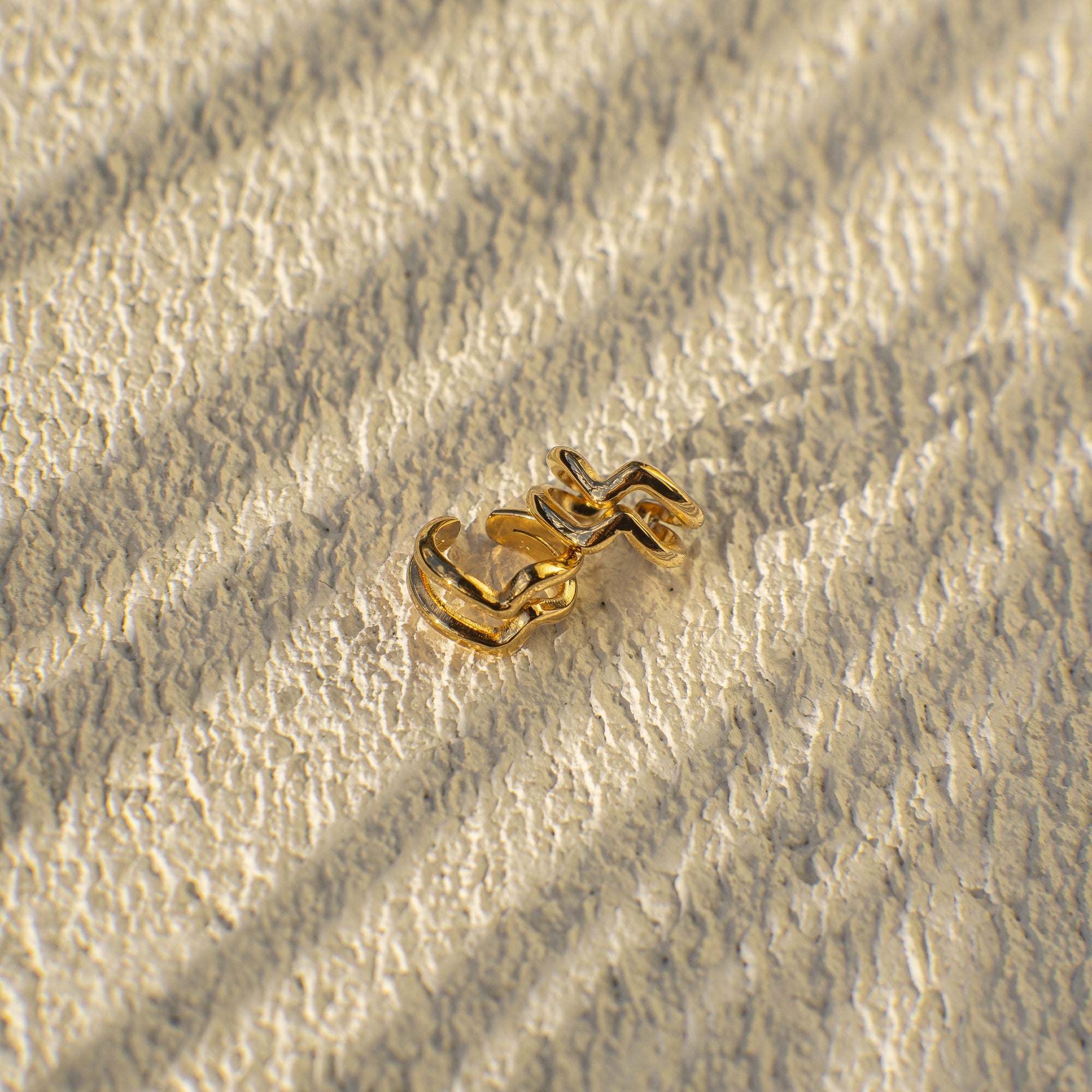 Gold chain earring on a textured beige surface