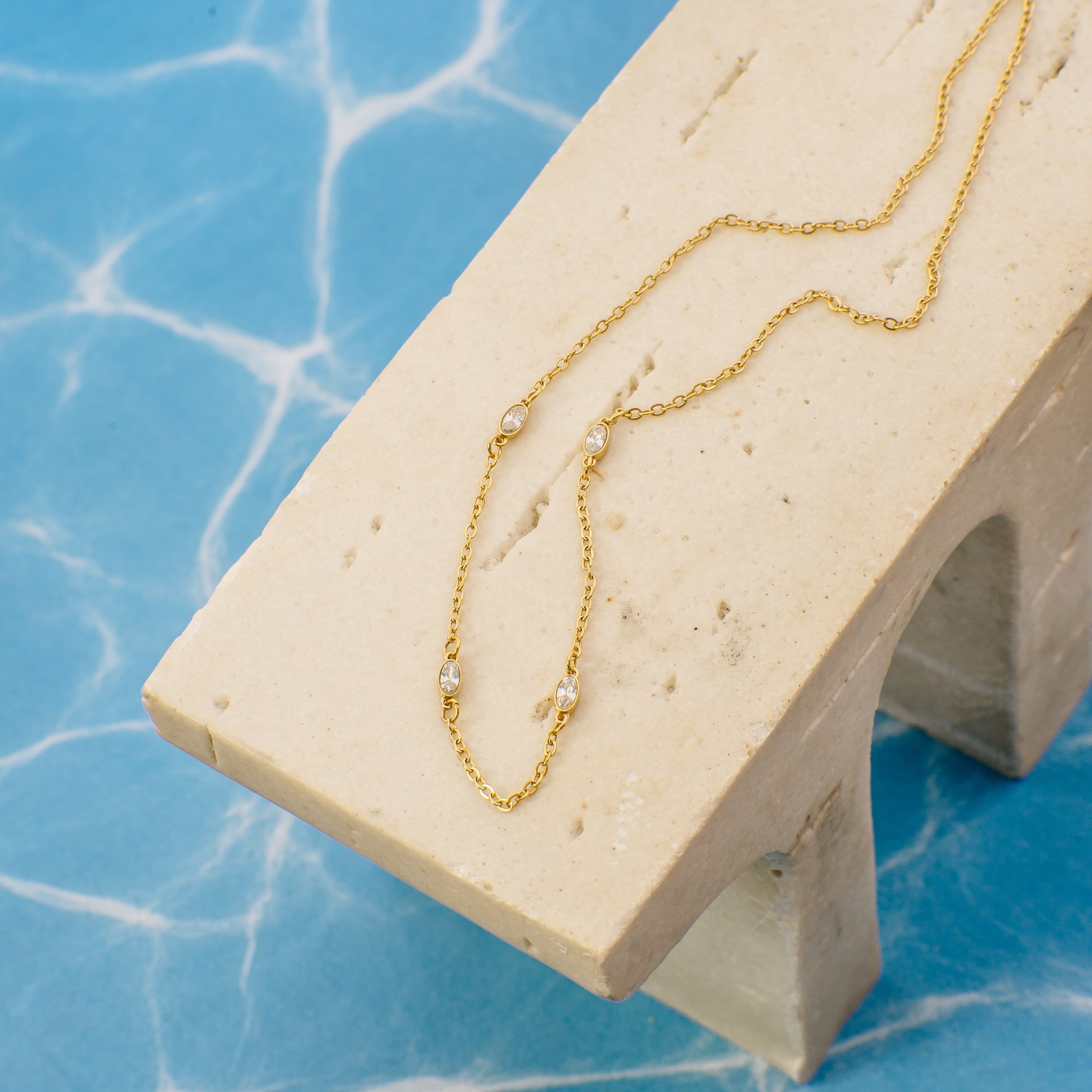 Gold necklace with small pearls on a beige stand against a blue marble background