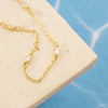 Gold chain necklace with clear stones on a beige stone surface with a blue tiled background