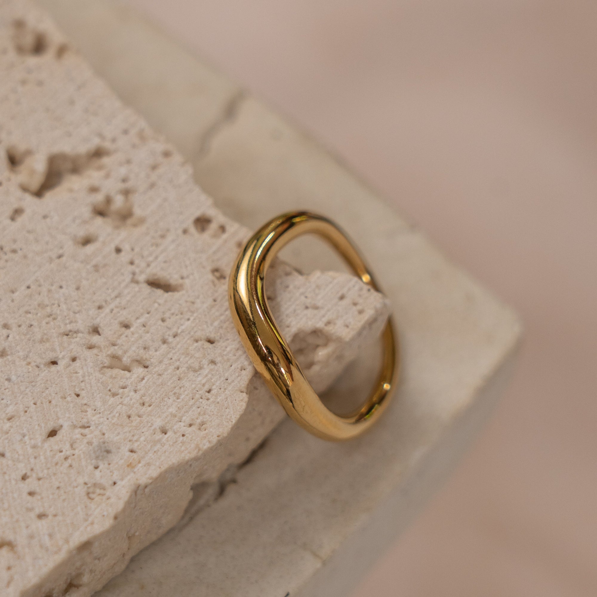 A gold-colored ring placed on a textured stone surface.