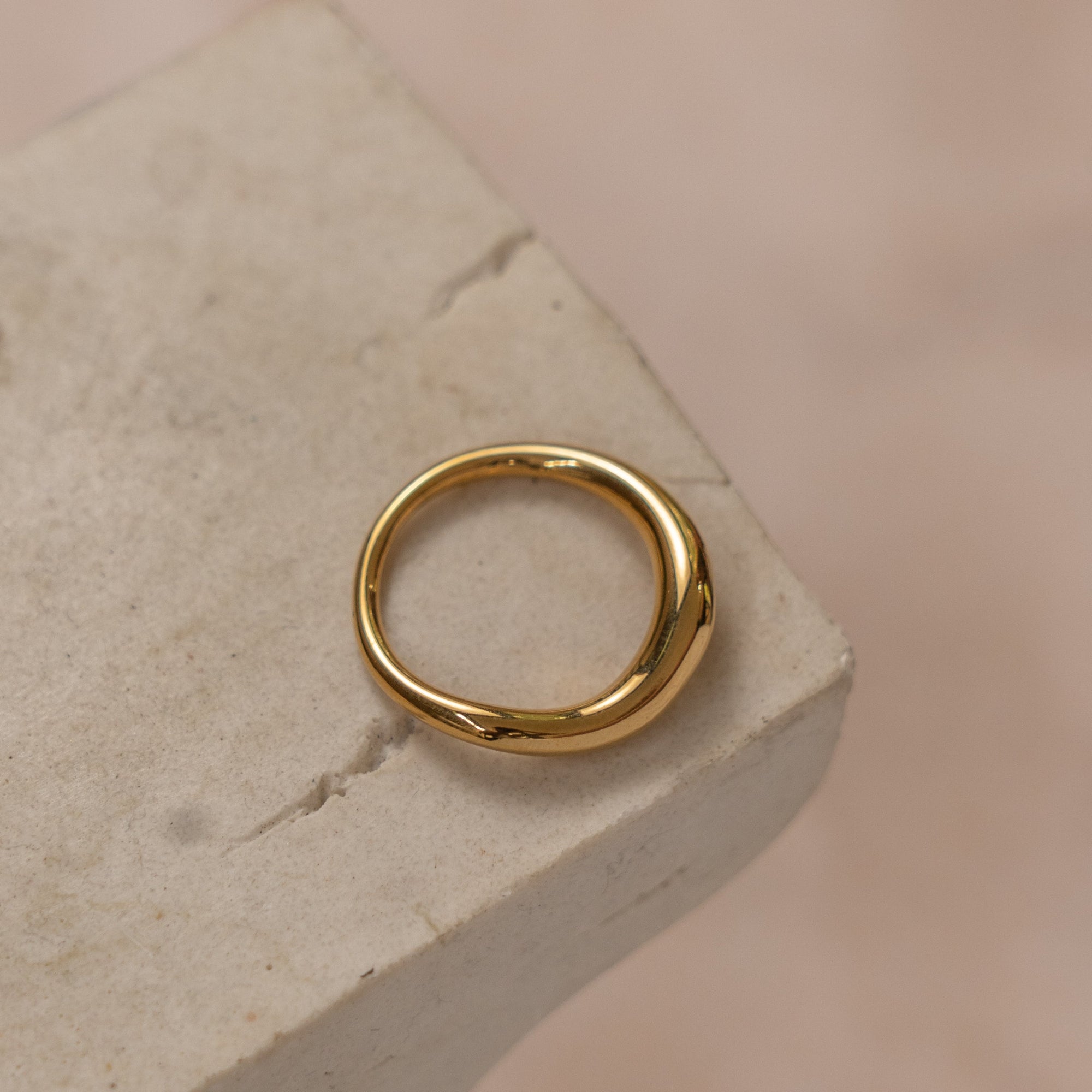 A gold-colored ring placed on a textured stone surface.