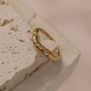 A gold-colored ring with multiple zirconia stones set on a textured surface.