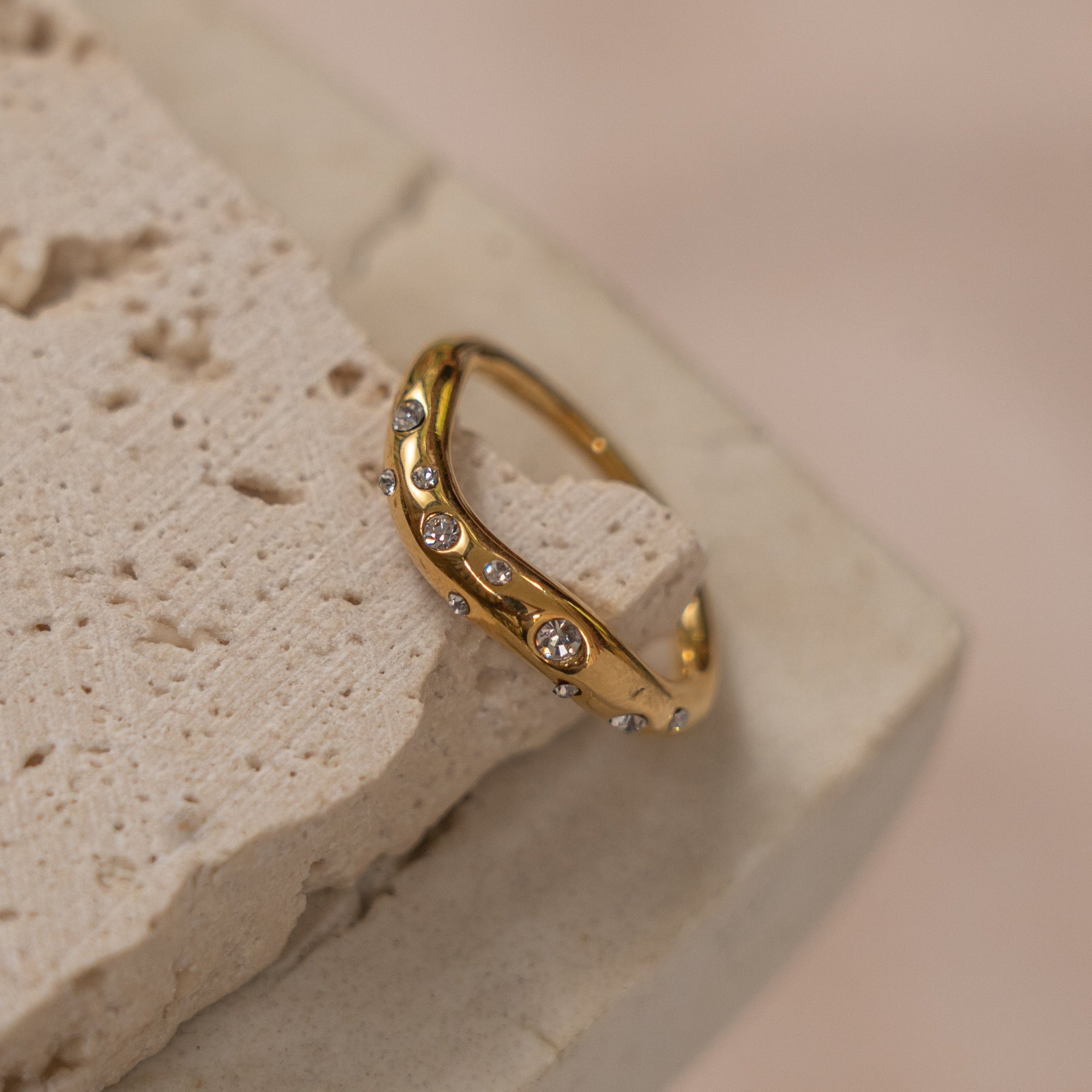 A gold-colored ring with multiple zirconia stones set on a textured surface.