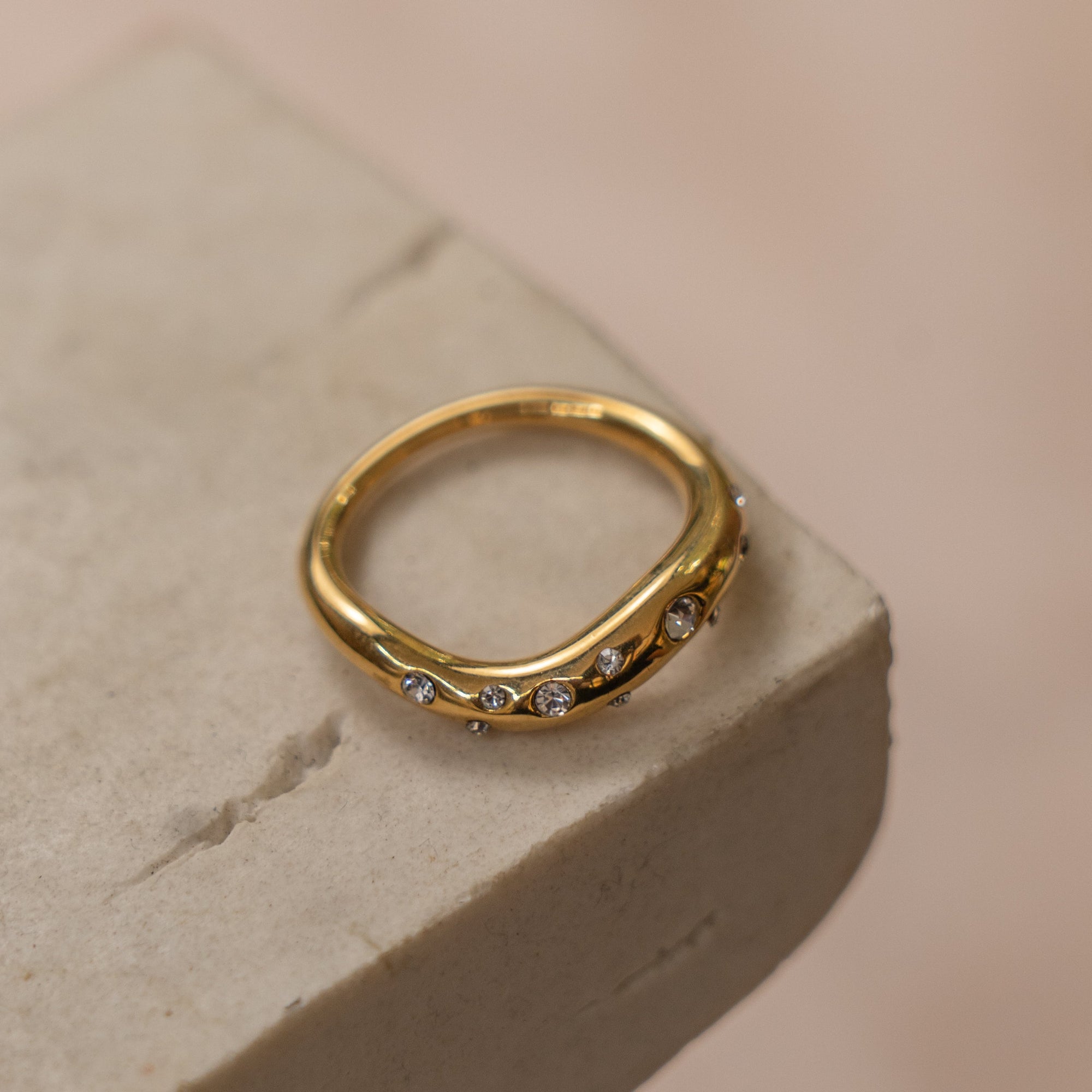 A gold-colored ring with multiple zirconia stones set on a textured surface.
