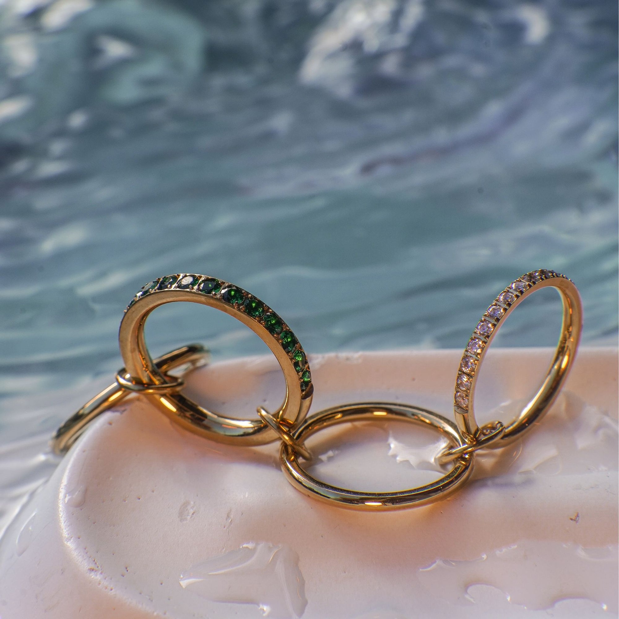 Gold rings with green and white stones on a shell with water background