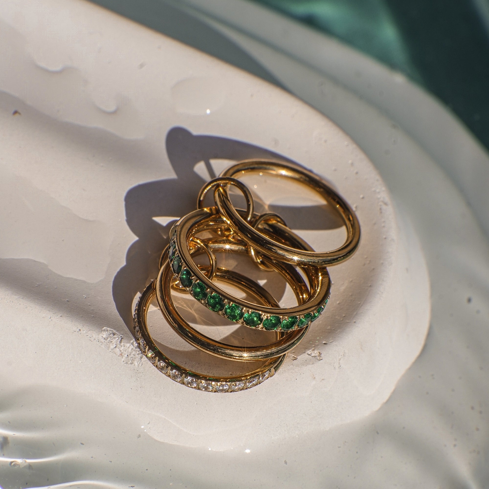 Three gold rings with green gemstones and clear stones on a white surface