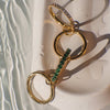 Gold equestrian bit with green stones on a textured white surface