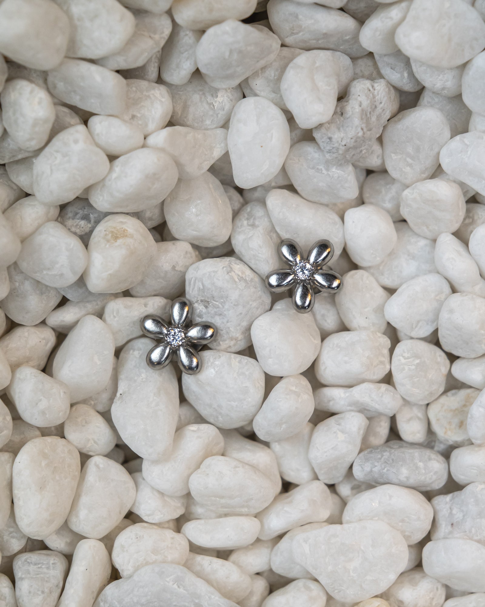 Silver flower-shaped earrings on a bed of small white stones