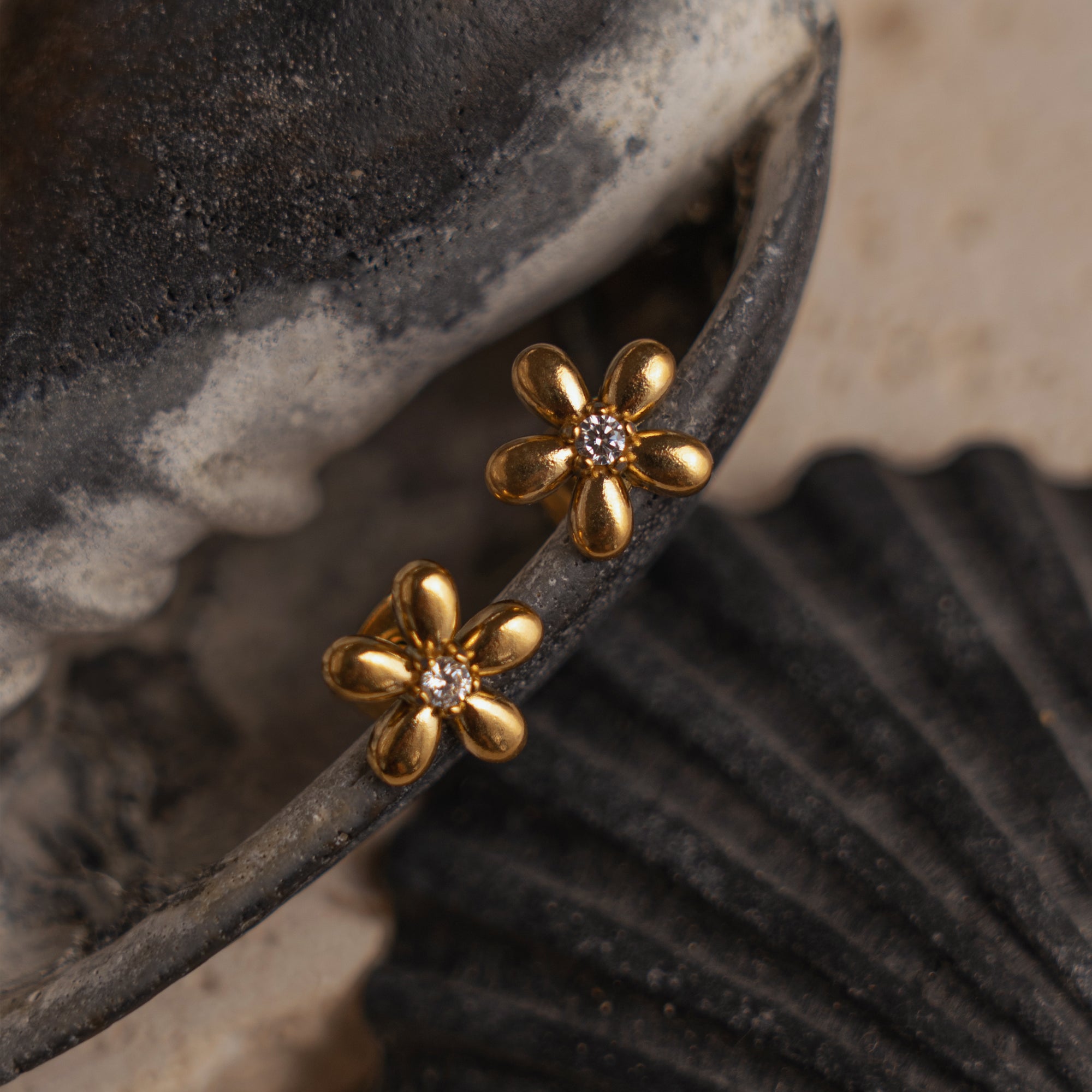 A pair of gold-colored floral stud earrings with sparkling zirconia detailing, placed on a textured surface.