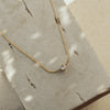 A dainty gold-colored necklace with a single zirconia pendant lying on a textured surface.