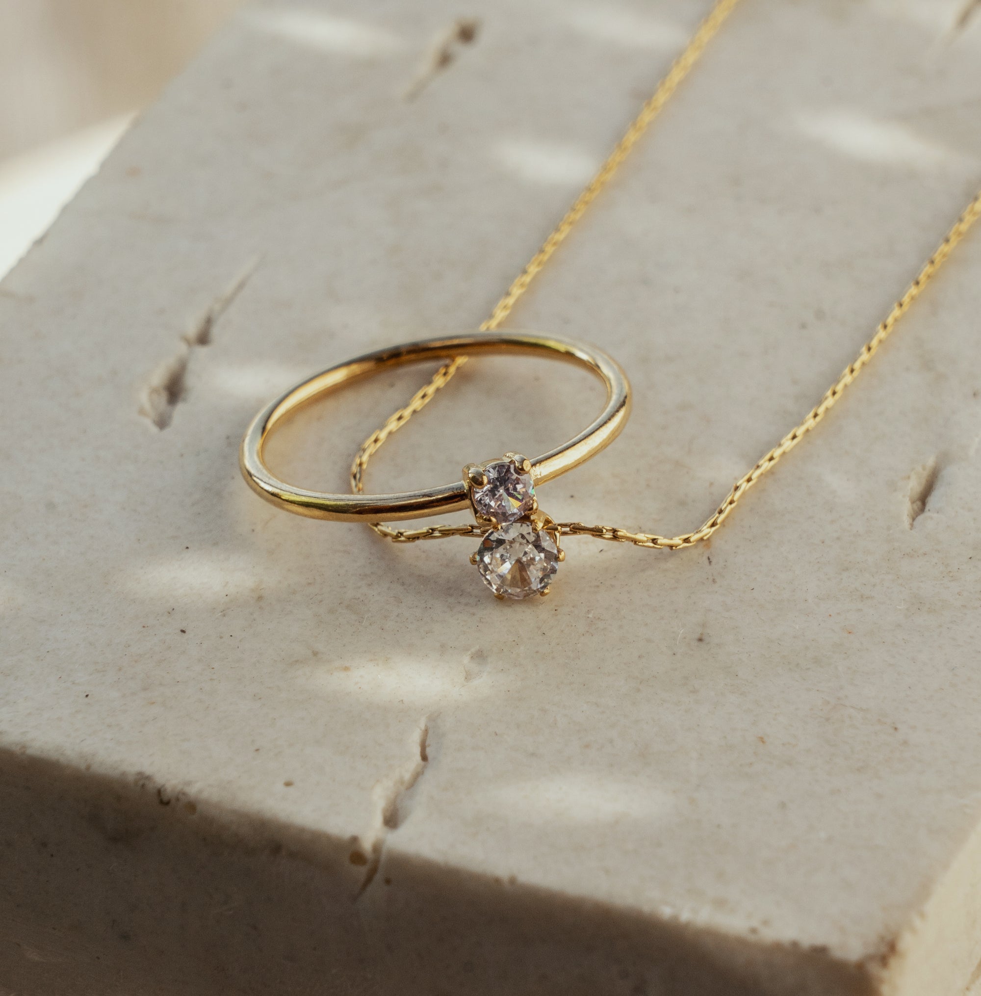 A gold necklace with cubic zirconia pendant paired with a ring that has the same style