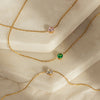A collection of Aurora gold necklaces with different pendant colors: rose quartz, emerald, and zirconia