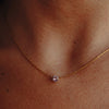 A gold necklace with rose quartz pendant on a model's neck