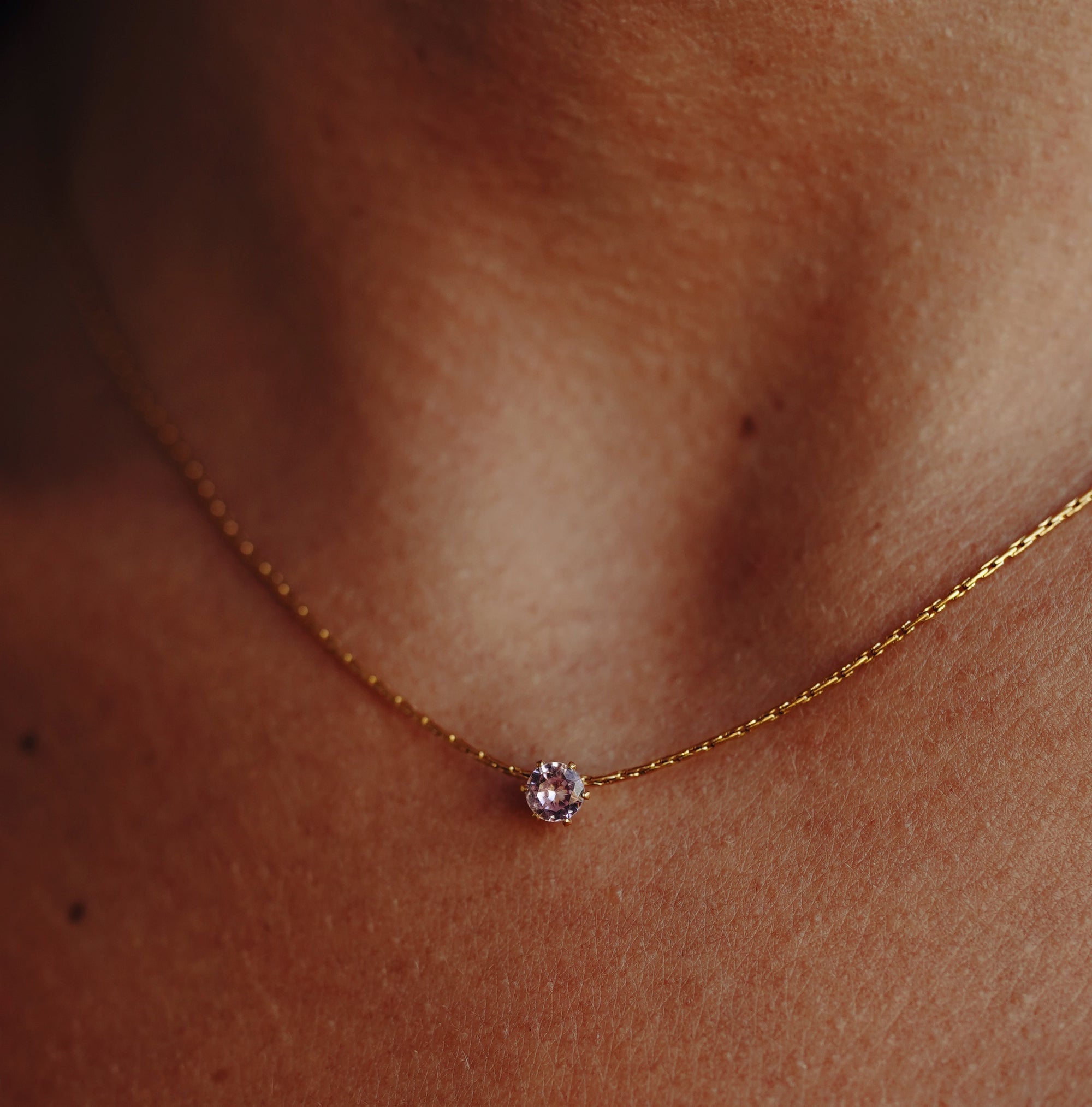 A gold necklace with rose quartz pendant on a model's neck