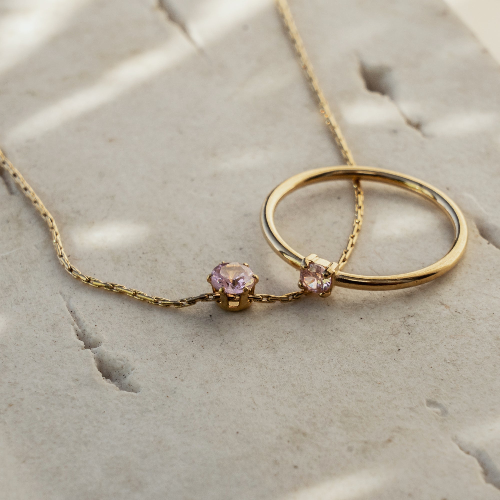 A gold necklace with rose quartz pendant paired with gold ring with rose quartz stone