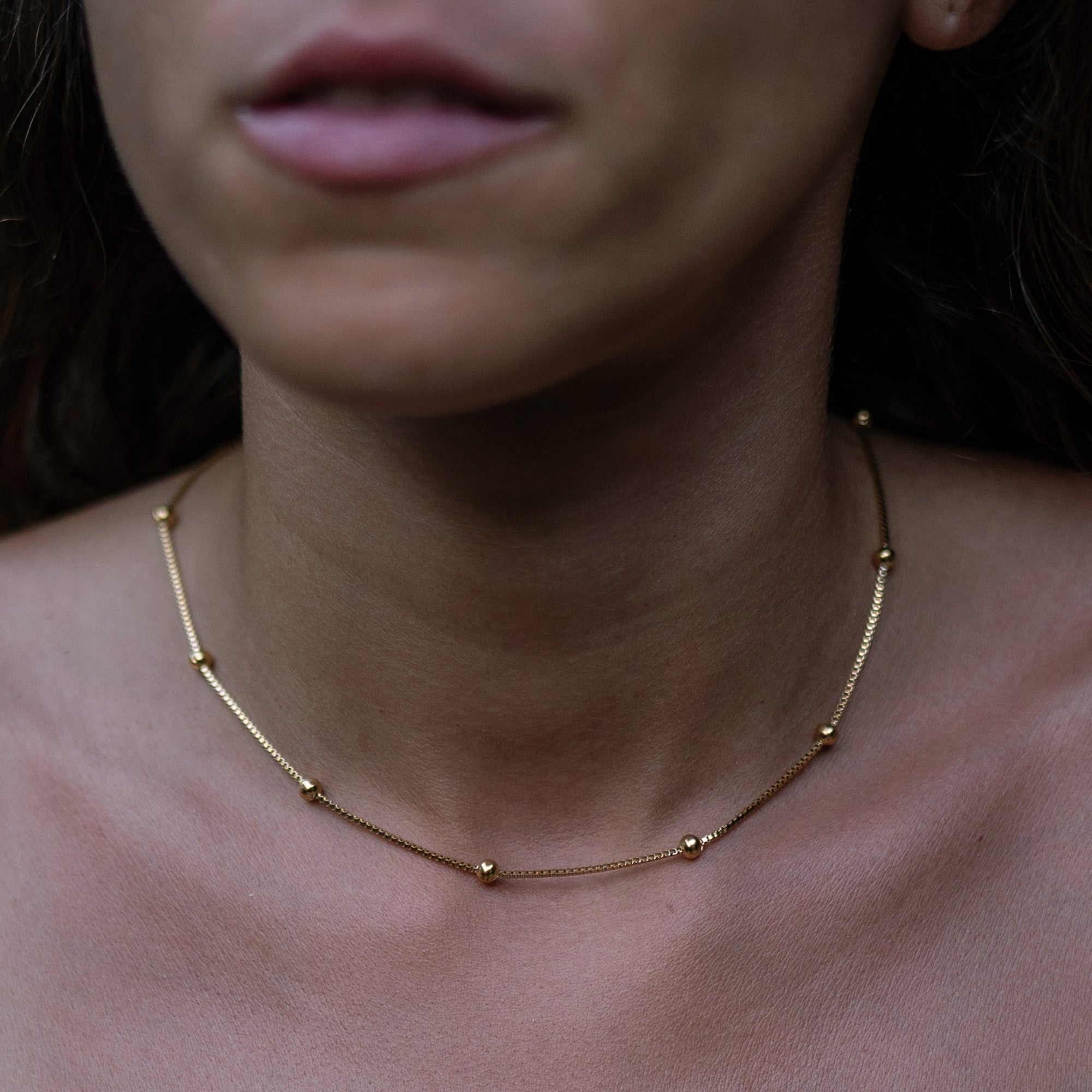 A woman wearing a gold necklace with little circle pendants.