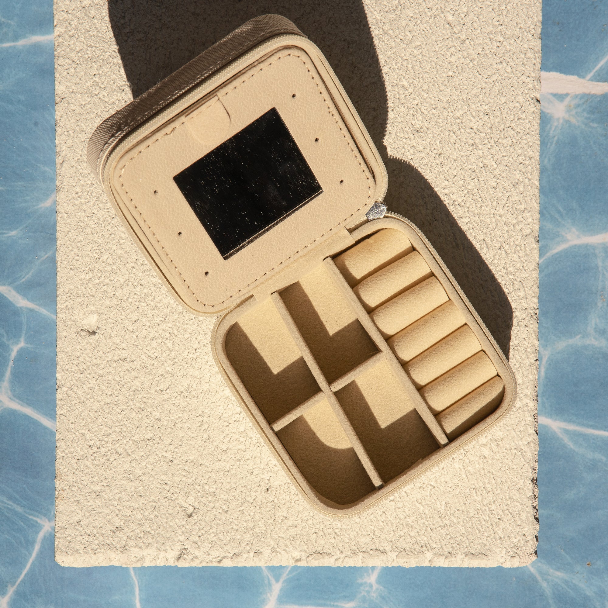 Beige jewellery case with compartments on a textured beige surface