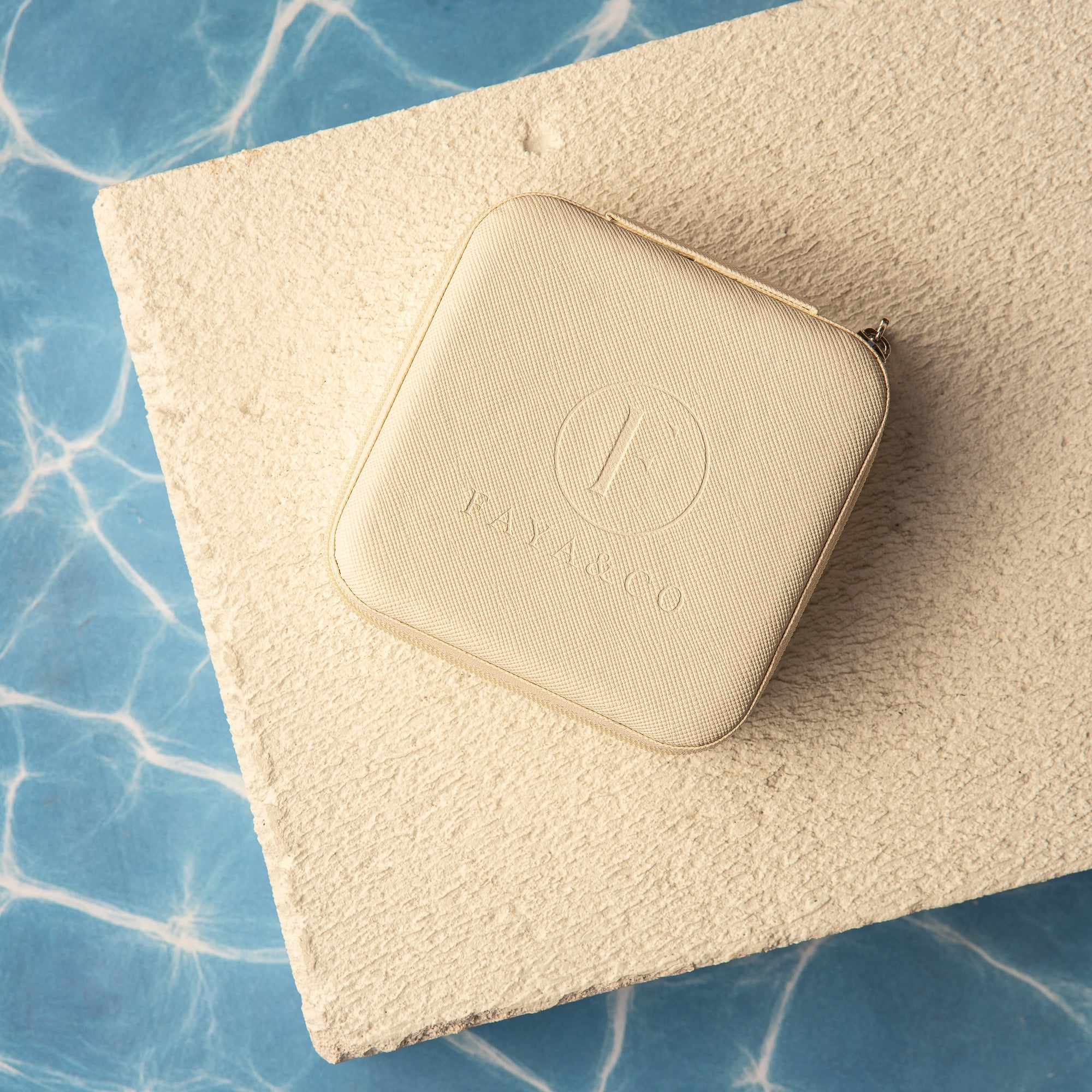 Beige jewellery case with a logo on a textured surface with blue water in the background