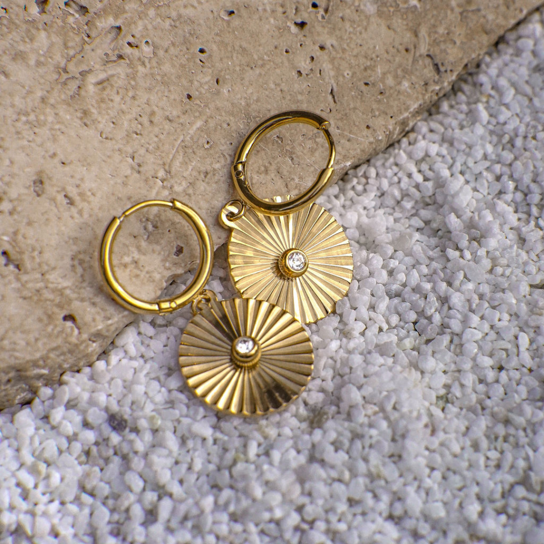 Gold hoop earrings with sunburst designs on a textured stone surface