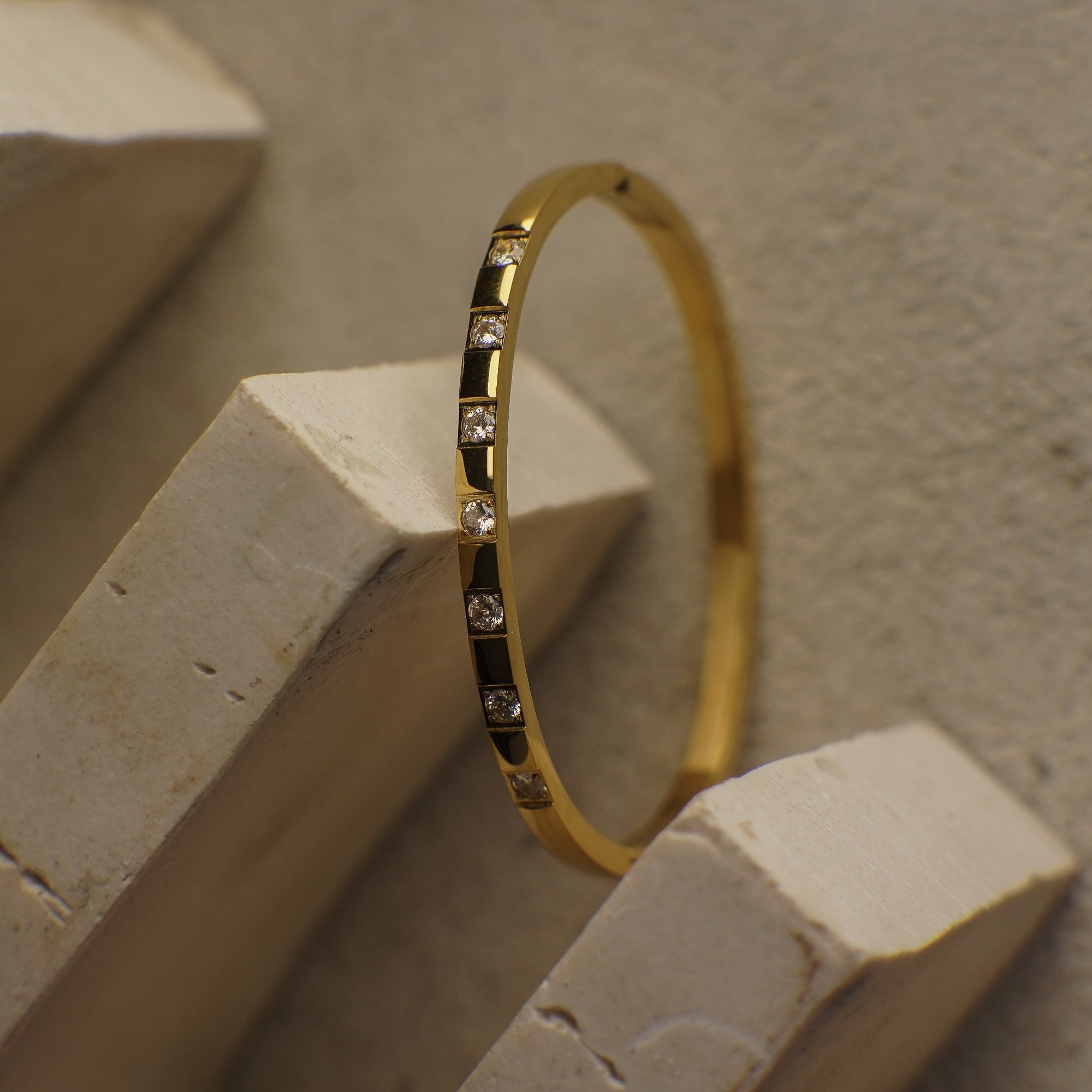 Gold bracelet with small diamonds on a beige stone surface