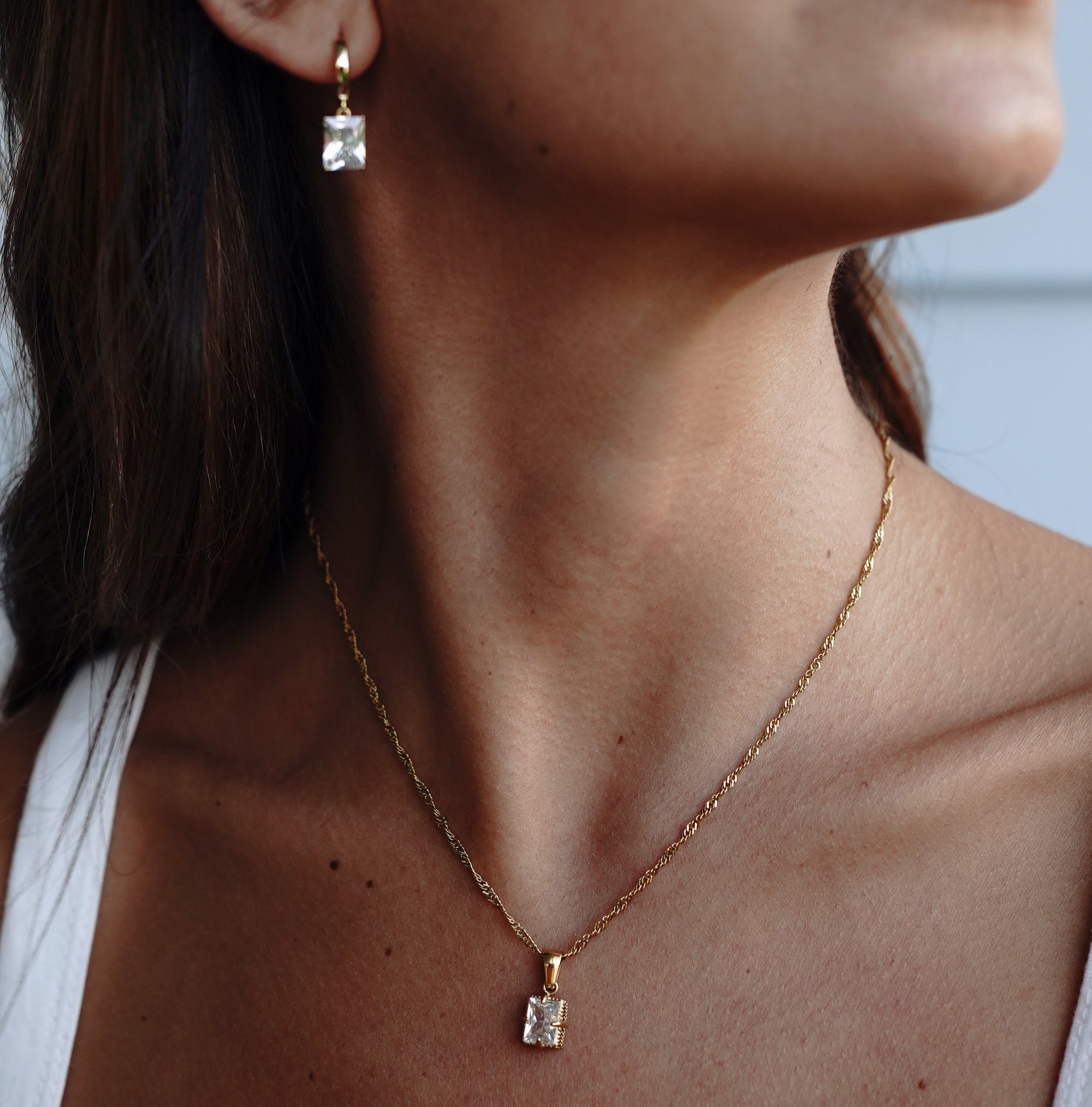 A model wearing a drop earring with cubic zirconia paired with gold necklace with the same design