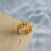 A gold-colored leaf ring placed on a textured surface with a water-like background.
