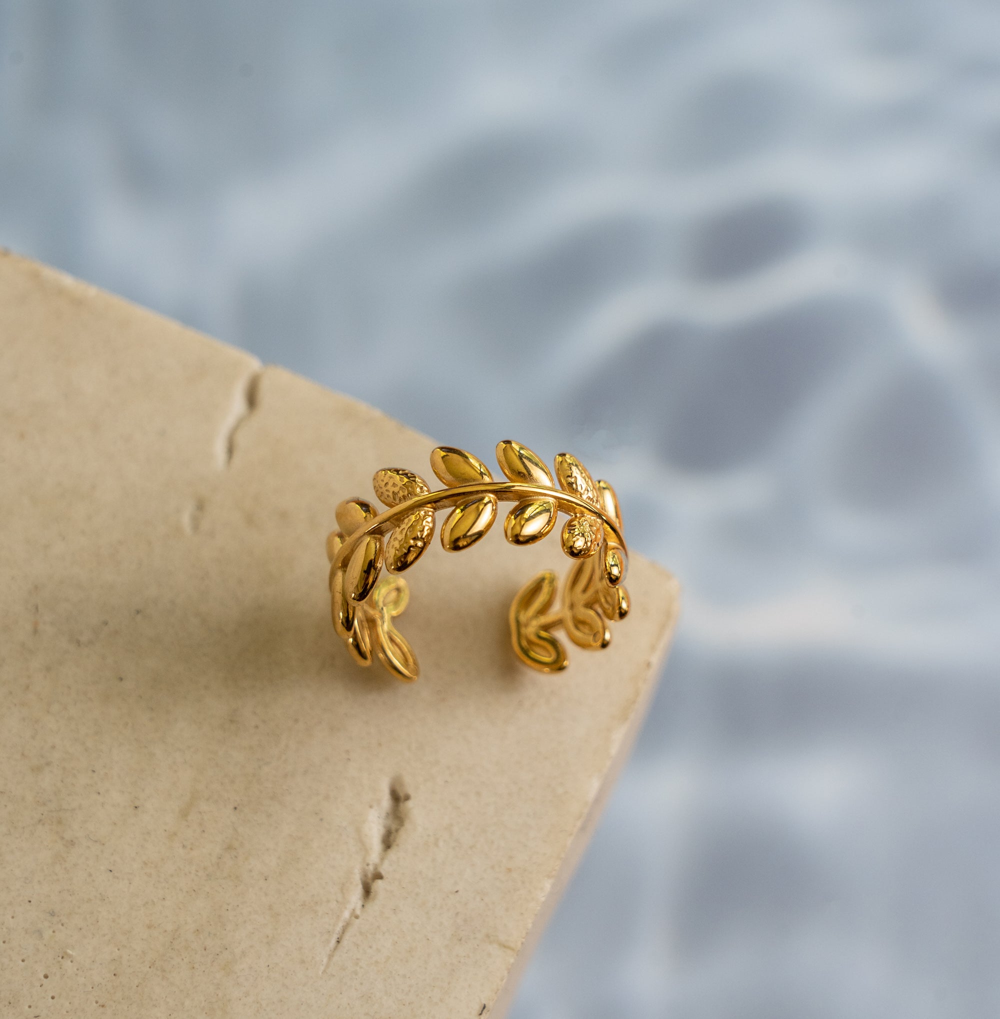 A gold-colored leaf ring placed on a textured surface with a water-like background.