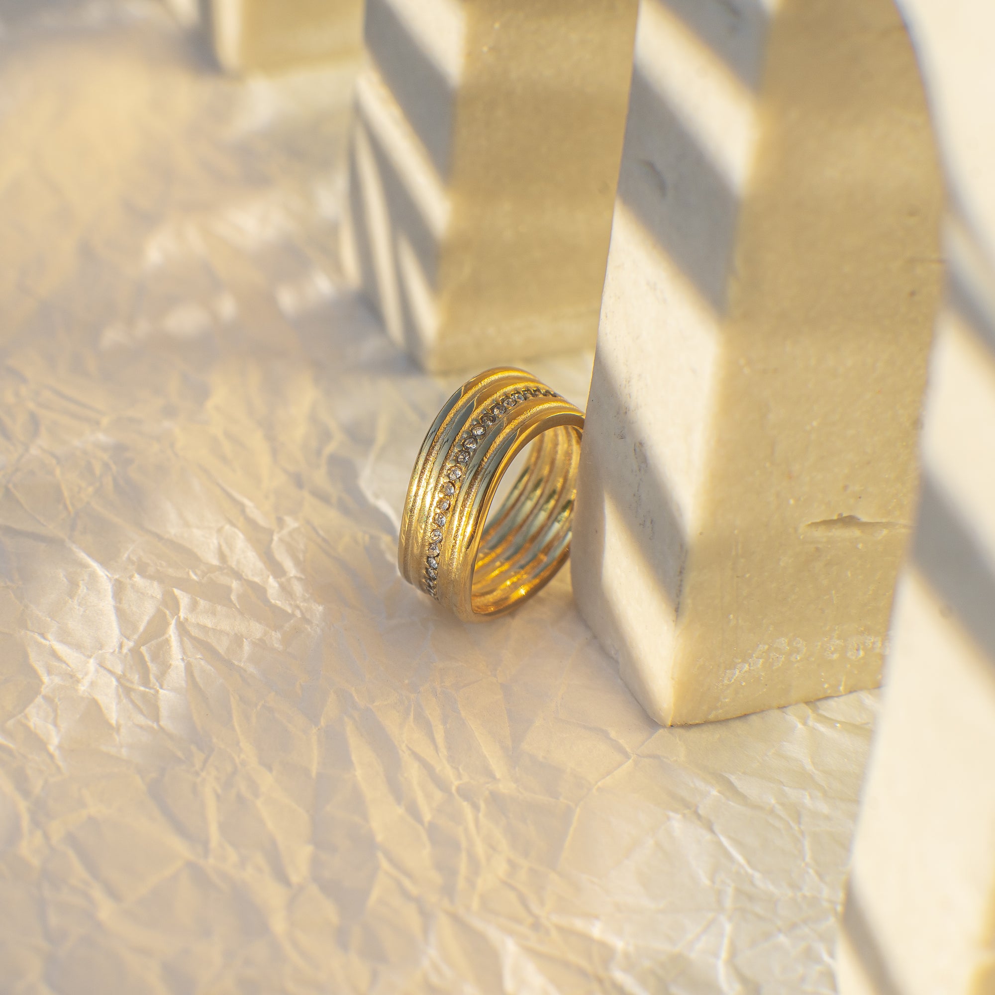 Gold ring on a textured beige surface with soft shadows