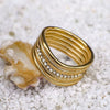 Gold ring with textured design and small stones on a white pebble surface
