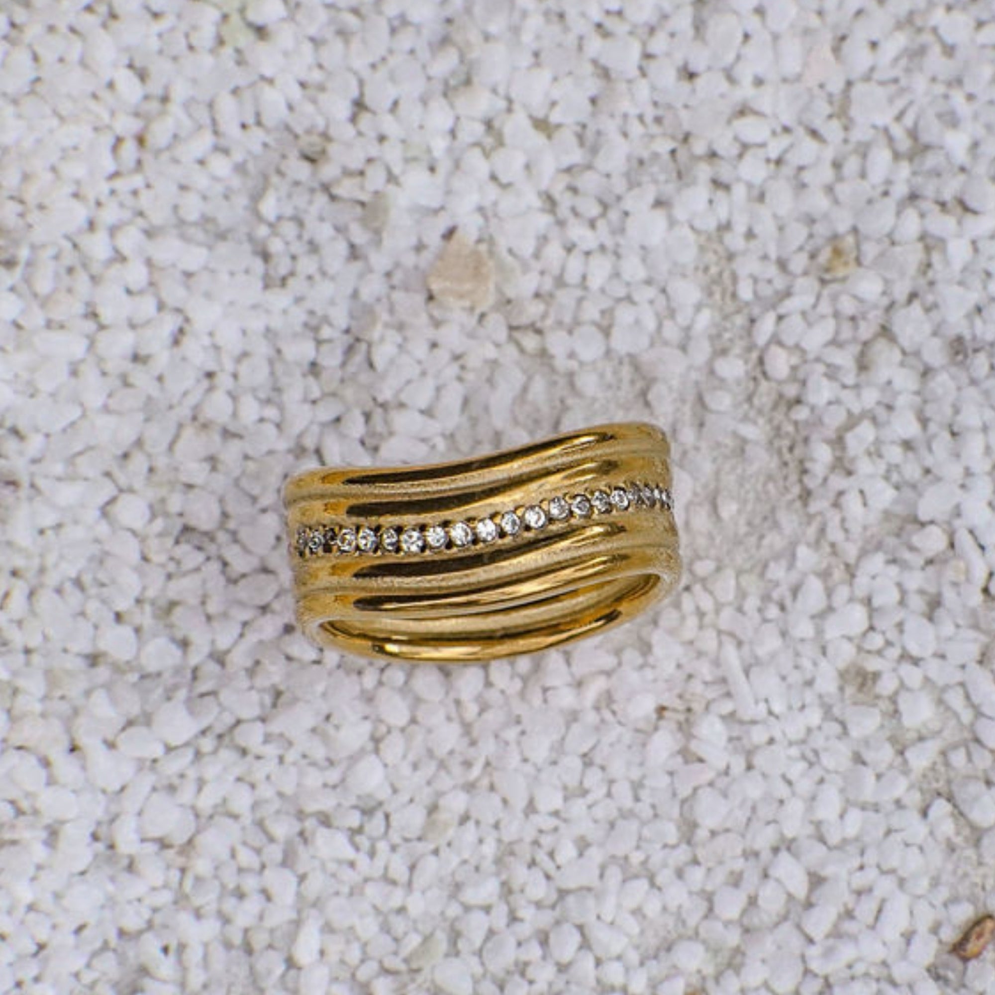 Gold ring with embedded diamonds on a textured beige surface