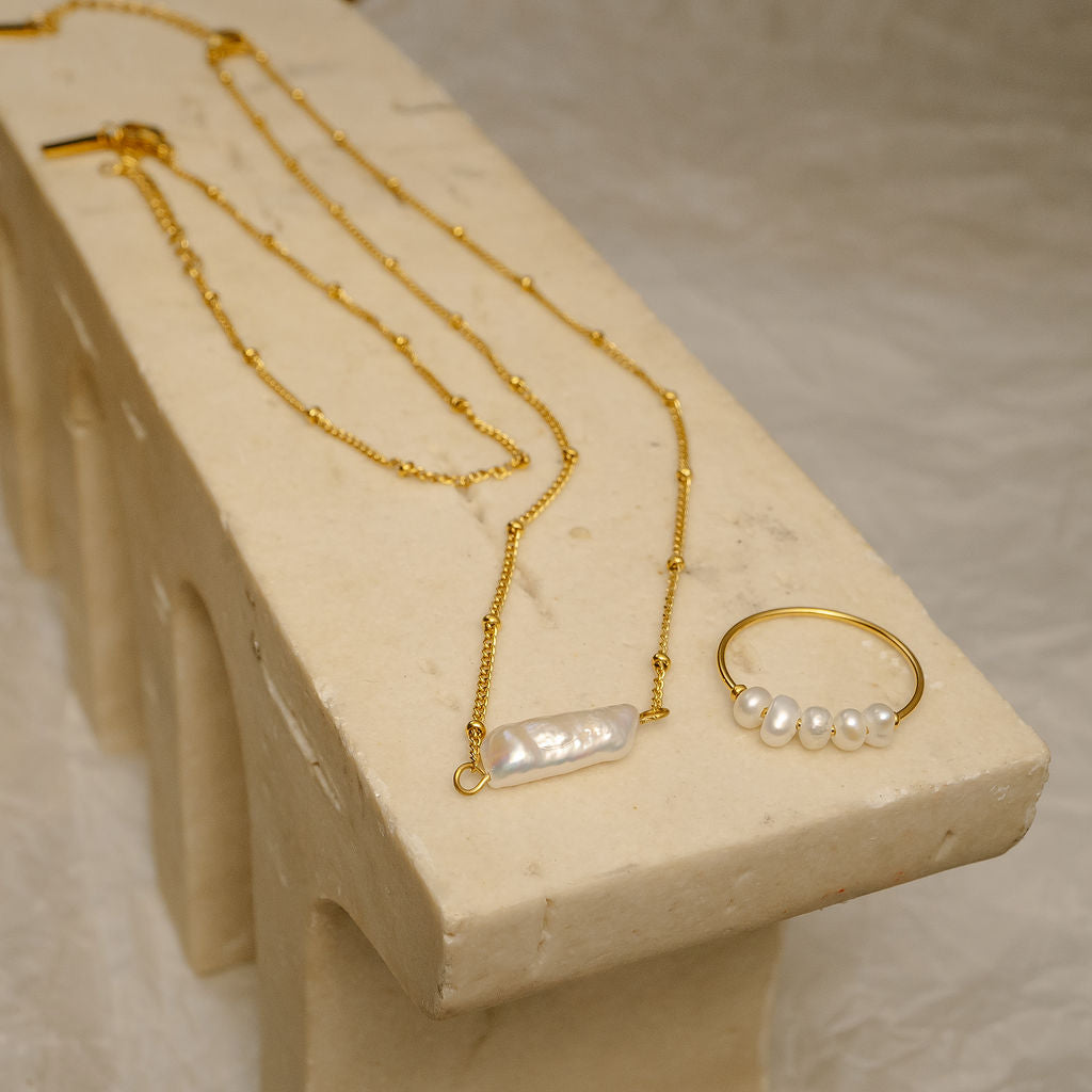 Gold necklace and ring with pearls on a stone surface