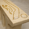 Gold necklaces and a ring with pearls on a beige stone surface
