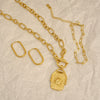 Gold necklace with pendant and hoop earrings on a beige textured background