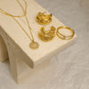 Gold necklace, earrings, and ring set on a beige stone surface