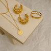 Gold jewelry set including necklace, hoop earrings, and ring on a beige surface.
