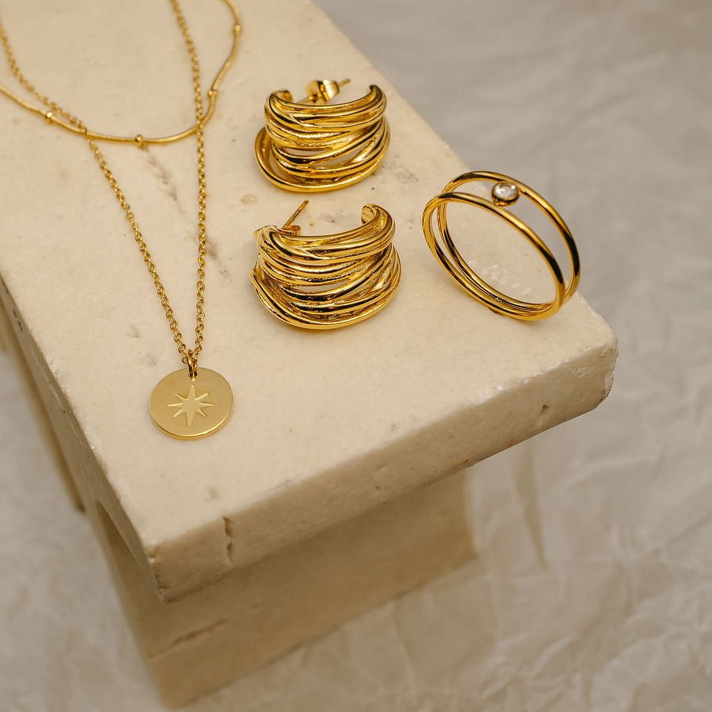 Gold jewelry set including necklace, earrings, and ring on a beige stone surface.