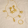Gold jewelry set with starfish and shell designs on a textured beige background