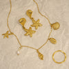 Gold jewelry set with starfish, shell, and pearl charms on a textured beige background