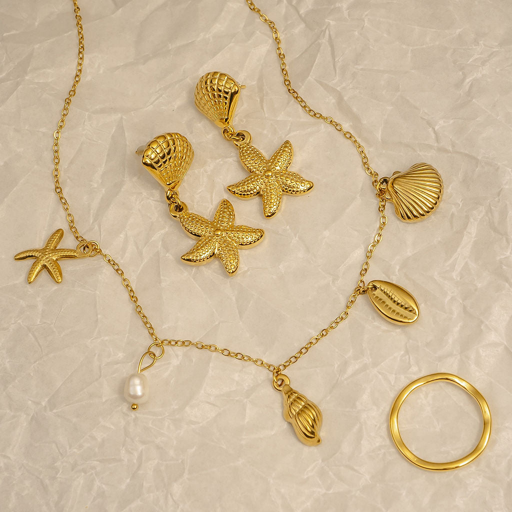 Gold jewelry set with starfish, shell, and pearl charms on a textured beige background