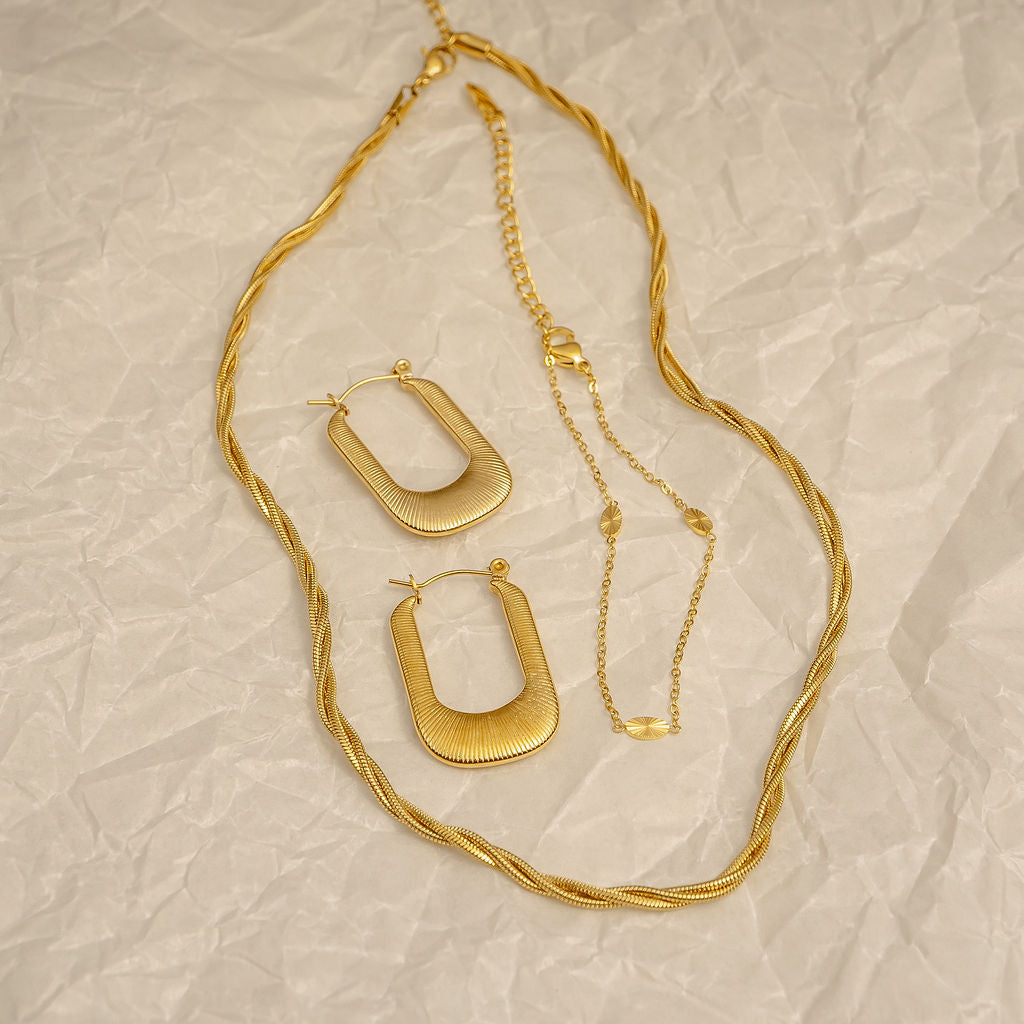 Gold necklace and hoop earrings on a textured beige surface