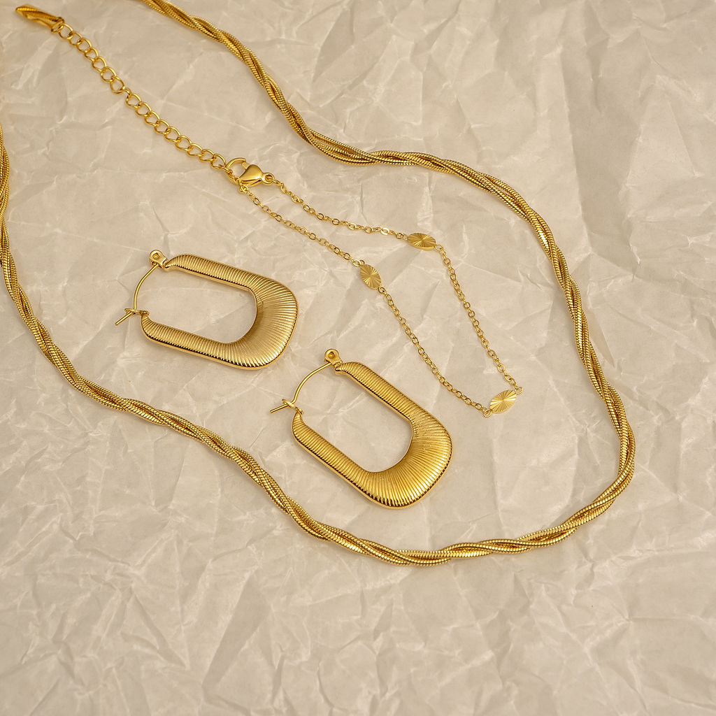 Gold necklace and hoop earrings on a textured beige surface