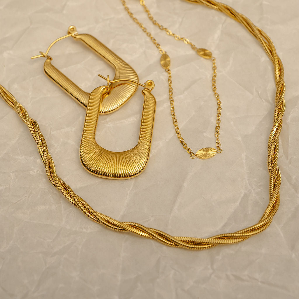 Gold hoop earrings and necklace on a textured beige surface