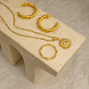 Gold hoop earrings and necklace on a beige stone block