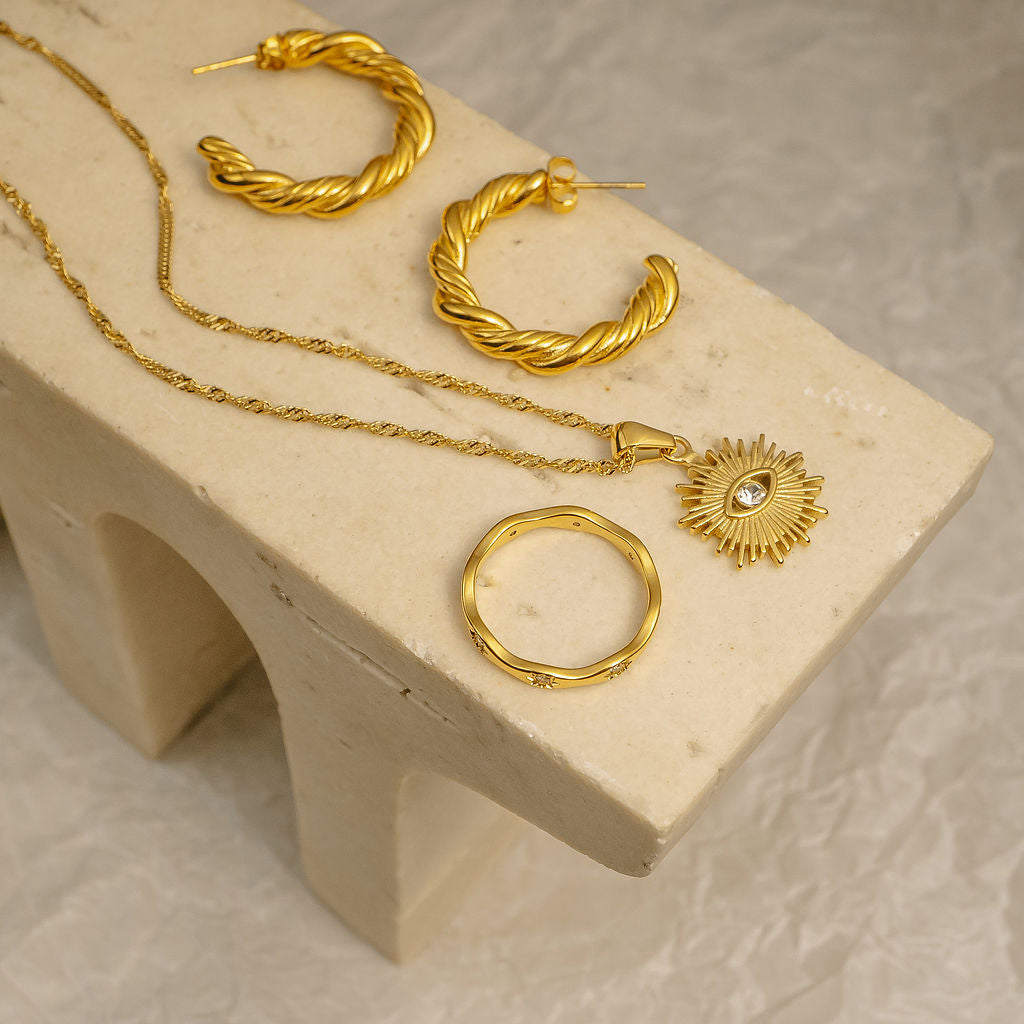 Gold hoop earrings and necklace on a beige stone block