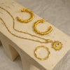 Gold jewelry set including hoop earrings and a necklace on a beige surface.