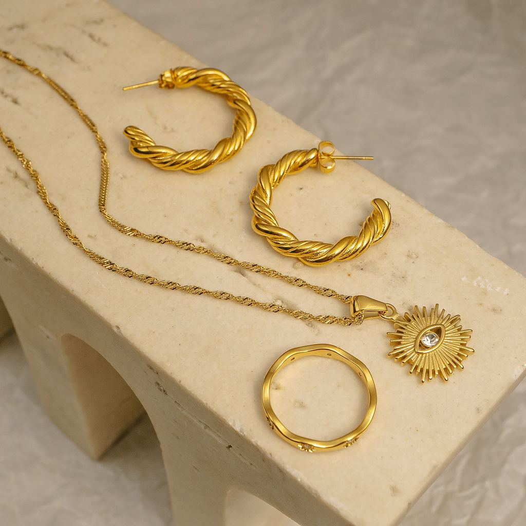 Gold jewelry set including hoop earrings and a necklace on a beige surface.