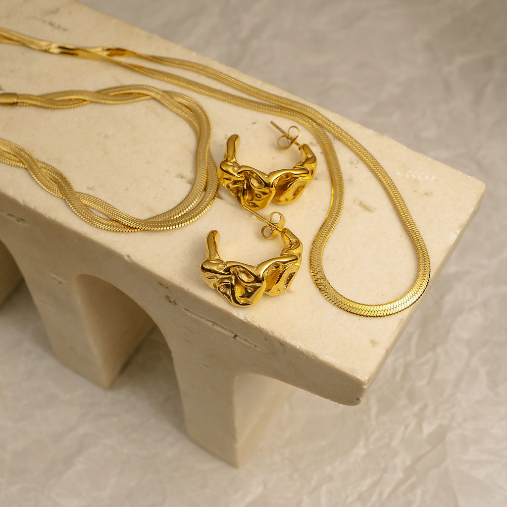 Gold jewelry set including necklace, earrings, and pendant on a beige stone surface.