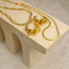 Gold necklace and earrings on a beige stone surface