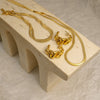 Gold necklace and earrings on a beige stone surface