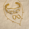 Gold bracelet with pearls and matching earrings on a beige textured background